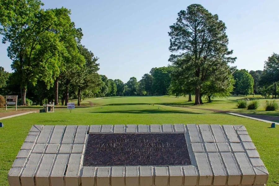 Stone plaque at the Back Acres driving range with tall pines behind